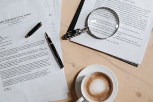 A top view of coffee and job application documents with a magnifying glass on a wooden desk.